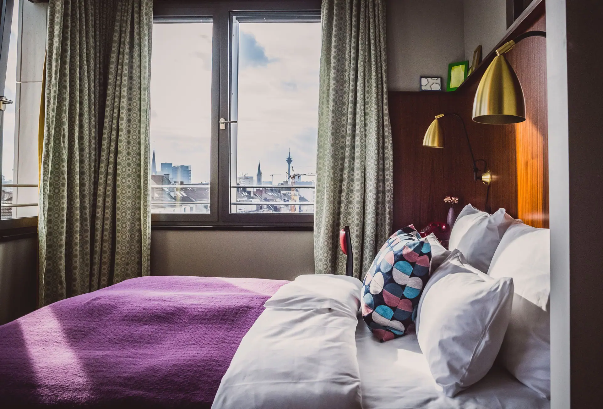 Bed met kussen en paarse deken in een kamer met een raam.