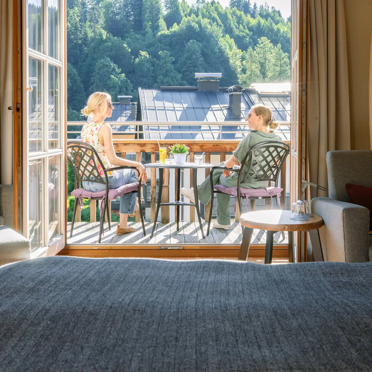 Twee vrouwen zitten op een balkon en kijken uit een raam.