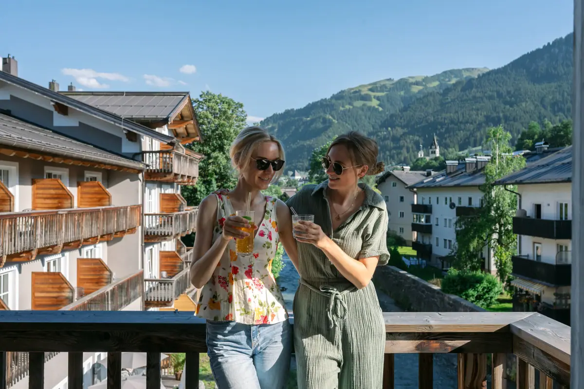 Twee vrouwen staan op een balkon met uitzicht op bergen en bomen.