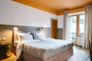 Een knus bed in een moderne hotelkamer in het HENRI Hotel Garmisch-Partenkirchen met toegang tot het balkon op de achtergrond.