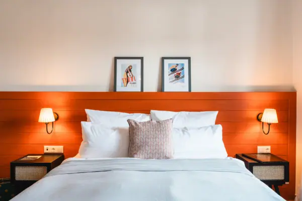 Hotelkamer HENRI Kitzbühel Een bed met een houten hoofdeinde en lampen.