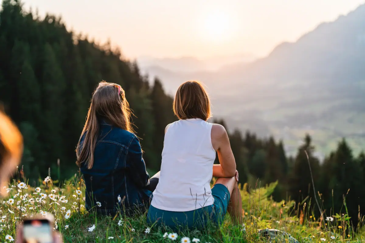 Uitzicht op de Kitzbüheler Alpen Twee vrouwen zitten op een heuvel en kijken naar de zonsondergang.