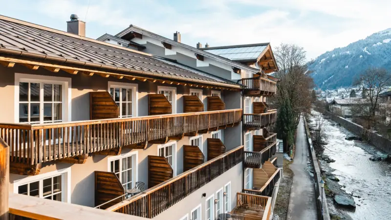 Hotelgebouw aan de rivier de Ache in Kitzbühel, met de bergen op de achtergrond.