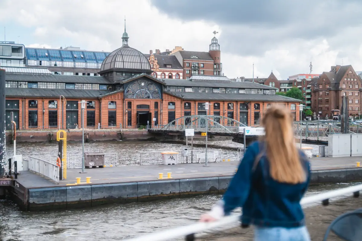 Een vrouw staat op een schip en kijkt naar een gebouw.