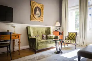 Klassieke hotelkamer in Wilhelminische stijl met een groen fluwelen bank, antiek bureau en statig portretschilderij aan de muur.