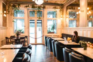 Een jonge vrouw werkt op haar laptop in de stijlvolle hotellobby van het HENRI Berlin, omringd door klassieke houten lambrisering, marmeren tafels en hangende groene planten in de Belle Époque stijl.