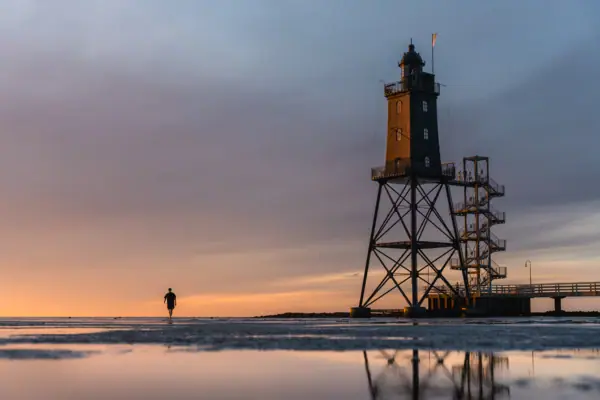 Er loopt iemand over het strand naast de vuurtoren van Obereversand.