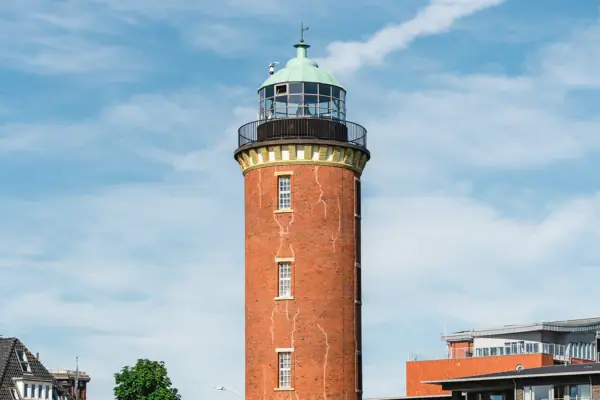 De Hamburgse vuurtoren in Cuxhaven met een groen dak en een gebouw op de achtergrond.