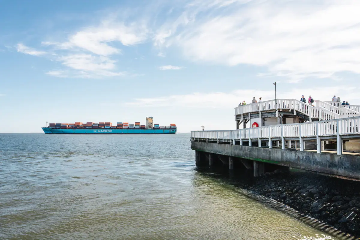 Een containerschip vaart op het water voor een steiger.